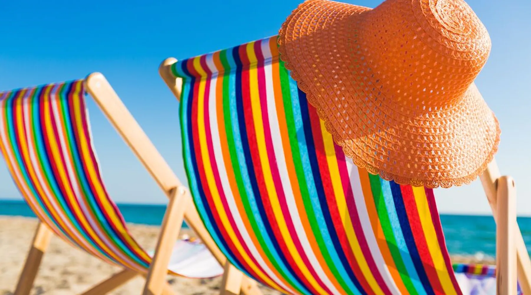 Chapeau de plage orange sur une chaise de plage colorée sur la plage