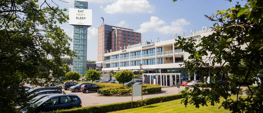 Vorderansicht des Van der Valk Hotels Eindhoven mit grünen Gärten und blauem Himmel
