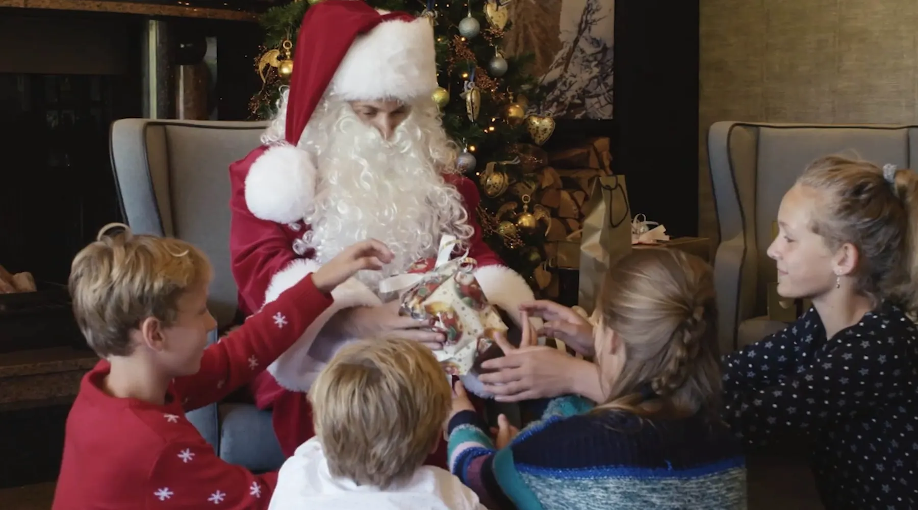 De Kerstman deelt cadeautjes uit aan kinderen bij een sfeervol versierde kerstboom.