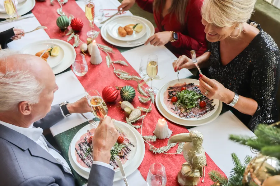 Een gezelschap geniet samen van gerechten aan een mooi gedekte kersttafel.