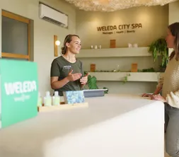 Eine Mitarbeiterin des WELEDA SPA bespricht die Wünsche eines Hotelgastes am Empfang des Salons.