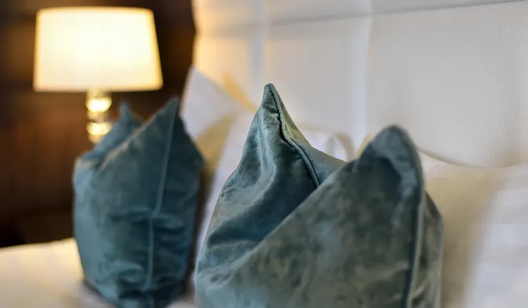 Detail van sfeervolle blauwe kussens op een comfortabel opgemaakt hotelbed voor een ontspannen zondagovernachting.