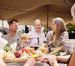 Eine Gruppe genießt gemeinsam eine Mahlzeit und die Gesellschaft der anderen unter einem großen Sonnenschirm auf der Terrasse.